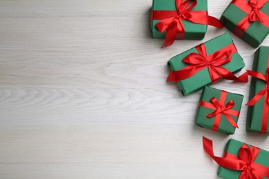 Photo of Many green gift boxes with red bows on white wooden table, flat lay. Space for text