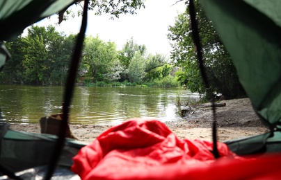 Camping tent with sleeping bag near lake, view from inside