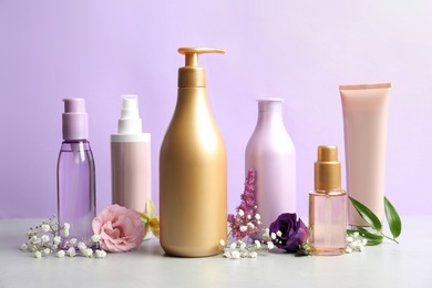 Photo of Set of hair cosmetic products and flowers on grey stone table against violet background