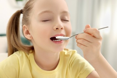 Photo of Cute little girl enjoying tasty yogurt indoors, closeup
