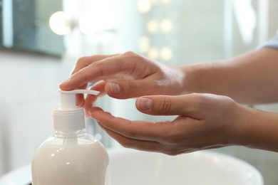 Photo of Woman applying liquid soap on hand in bathroom, closeup