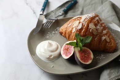 Photo of Delicious croissant with fig, almond flakes and cream on white table, closeup