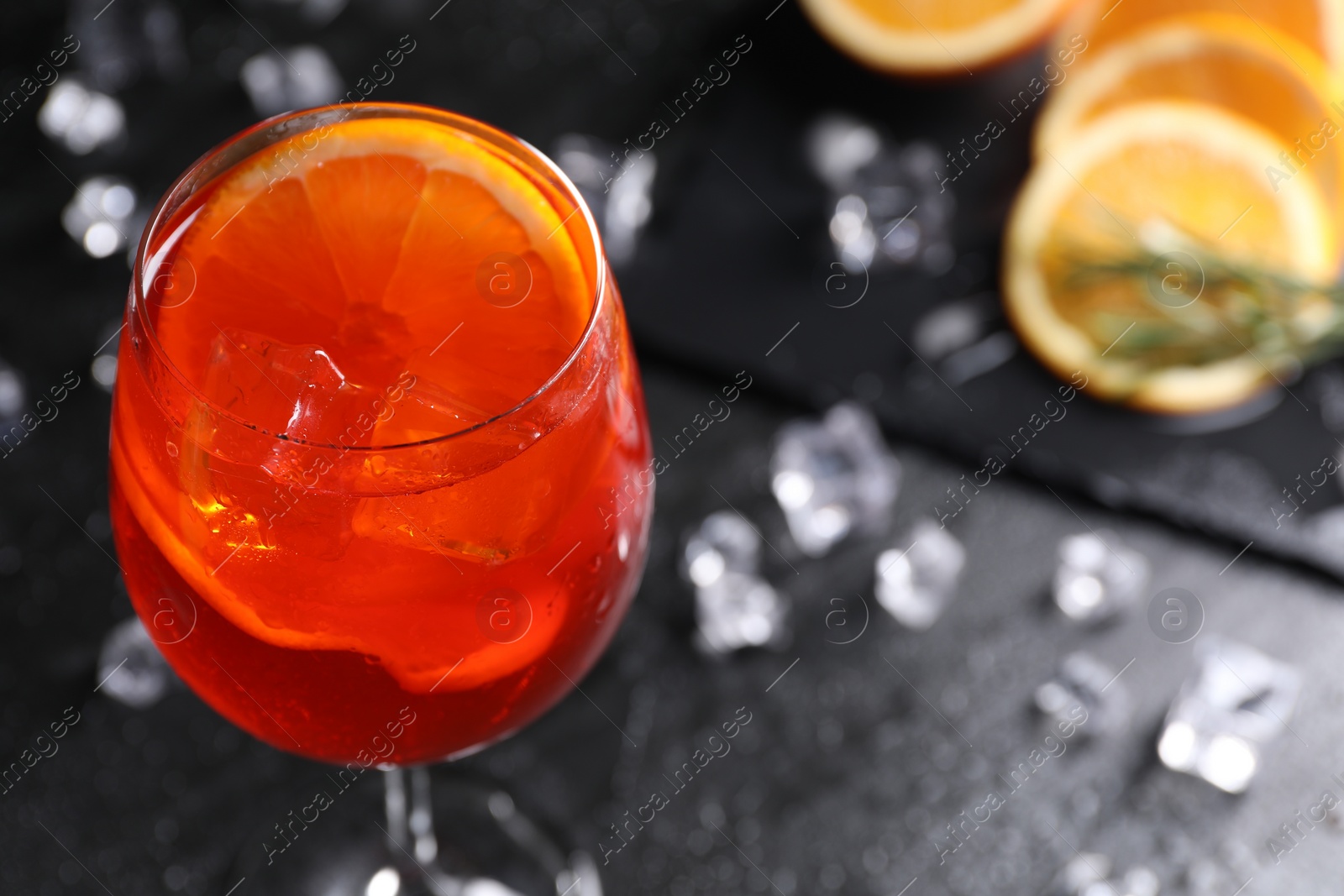 Photo of Glass of tasty Aperol spritz cocktail with orange slices and ice cubes on dark gray table, closeup. Space for text