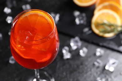 Glass of tasty Aperol spritz cocktail with orange slices and ice cubes on dark gray table, closeup. Space for text