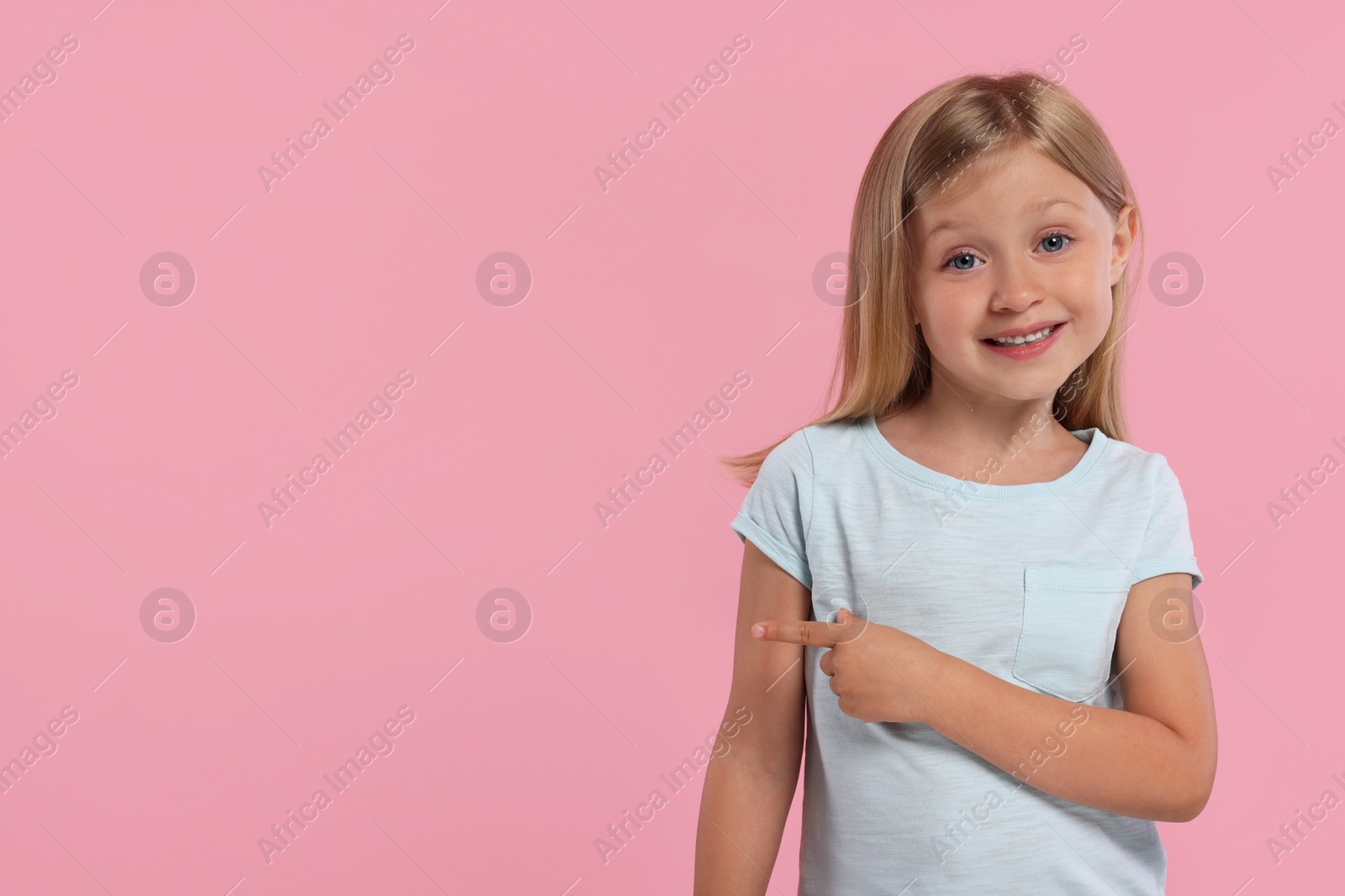 Photo of Special promotion. Little girl pointing at something on pink background. Space for text