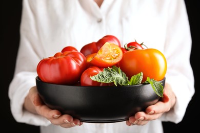 Photo of Woman holding bowl with fresh ripe tomatoes on black background, closeup