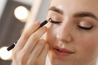 Makeup product. Woman applying black eyeliner indoors, closeup