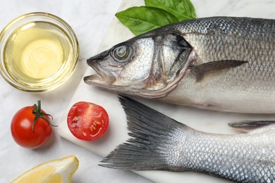 Photo of Sea bass fish and ingredients on white marble table, flat lay