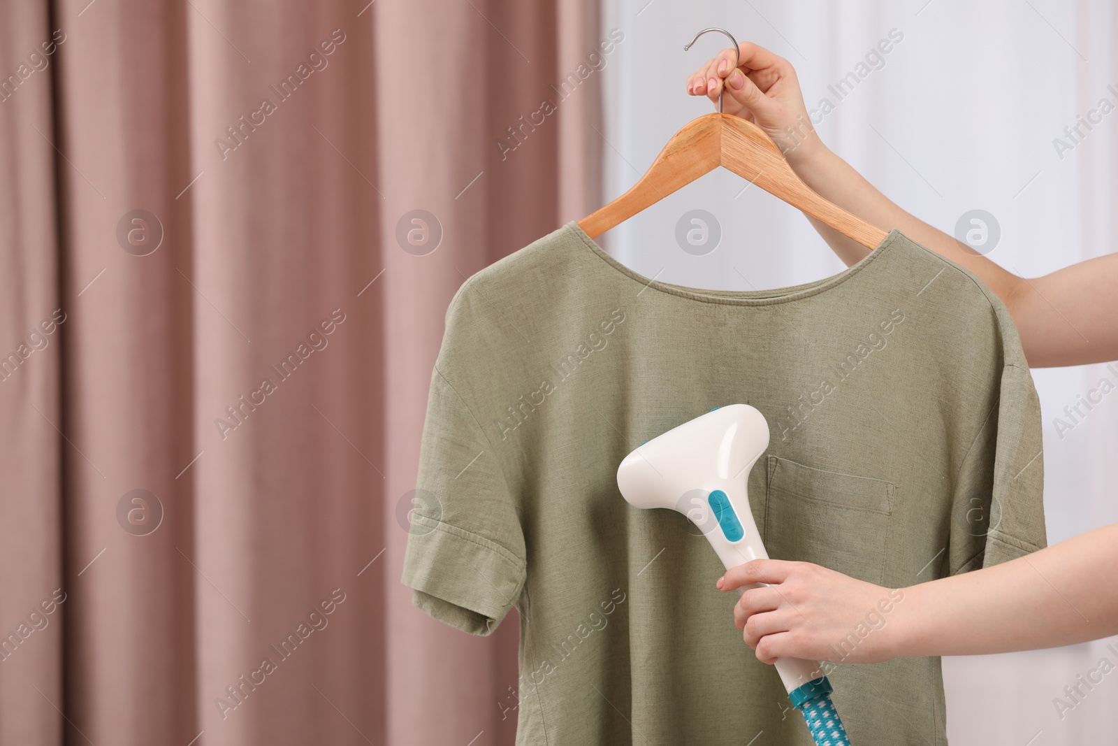 Photo of Woman steaming T-shirt on hanger at home, closeup. Space for text