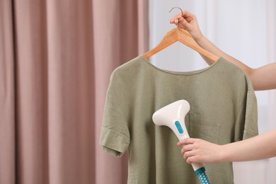Woman steaming T-shirt on hanger at home, closeup. Space for text