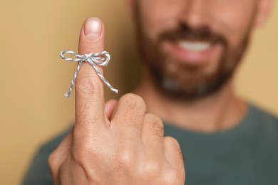 Photo of Man showing index finger with tied bow as reminder against beige background, focus on hand