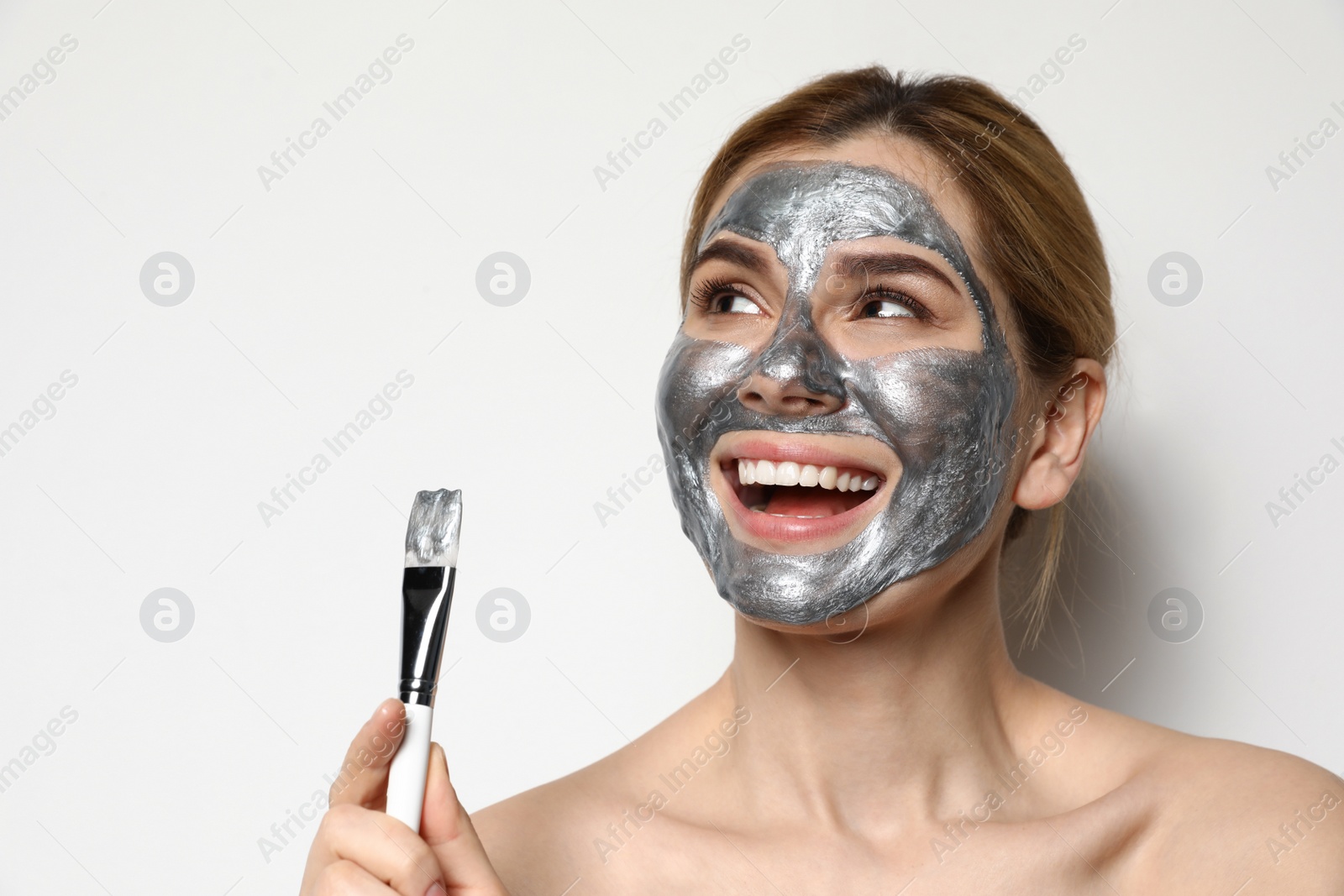 Photo of Beautiful woman applying mask onto face against light background