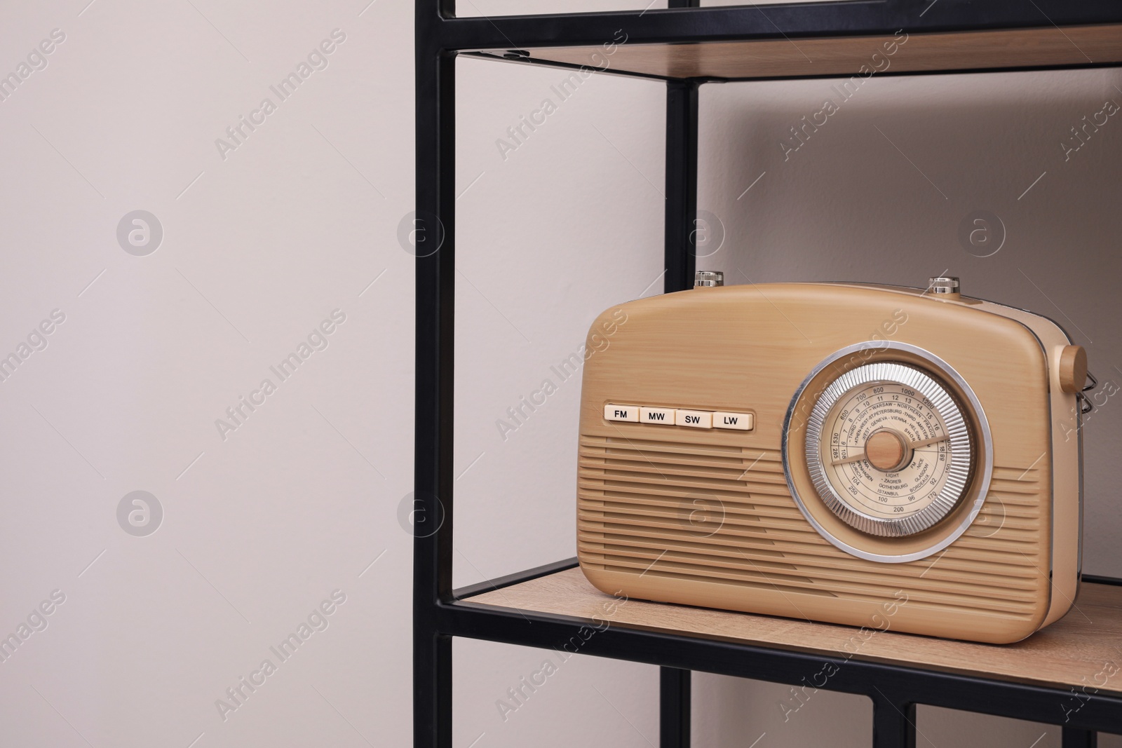 Photo of Stylish beige radio on rack near light wall indoors, space for text