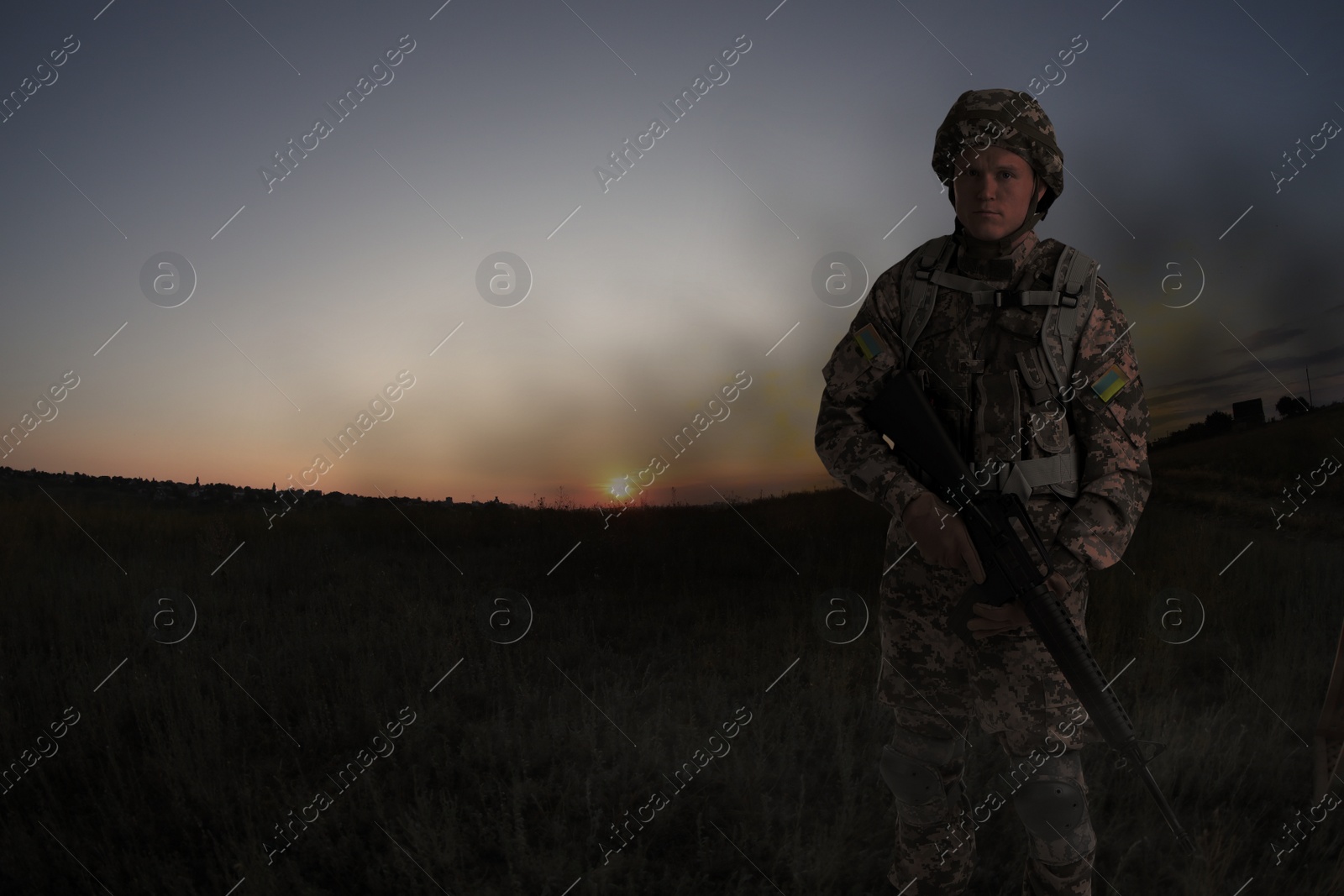 Image of Ukrainian soldier with machine gun on battlefield at sunset