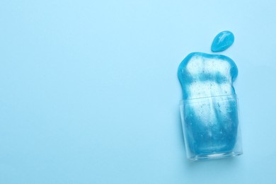 Photo of Overturned plastic container with bright slime on light blue background, top view. Space for text