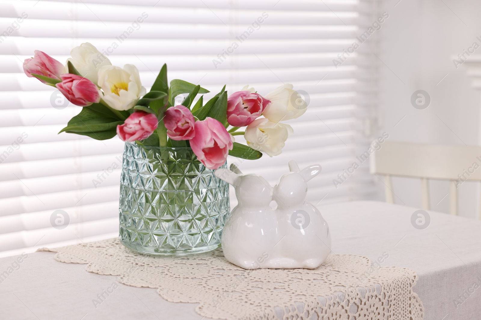 Photo of Easter decorations. Bouquet of tulips in vase and bunny figures on white table at home