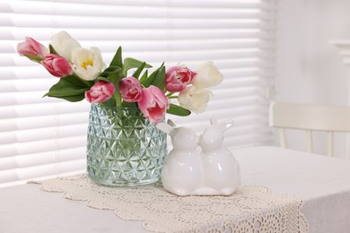 Easter decorations. Bouquet of tulips in vase and bunny figures on white table at home