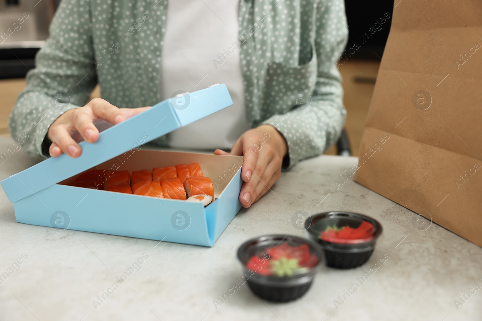 Photo of Woman unpacking her order from sushi restaurant at table in kitchen, closeup