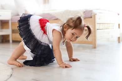 Adorable little baby girl trying to stand up in room