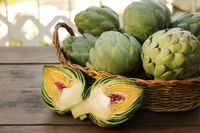 Photo of Wicker basket with fresh raw artichokes on wooden table