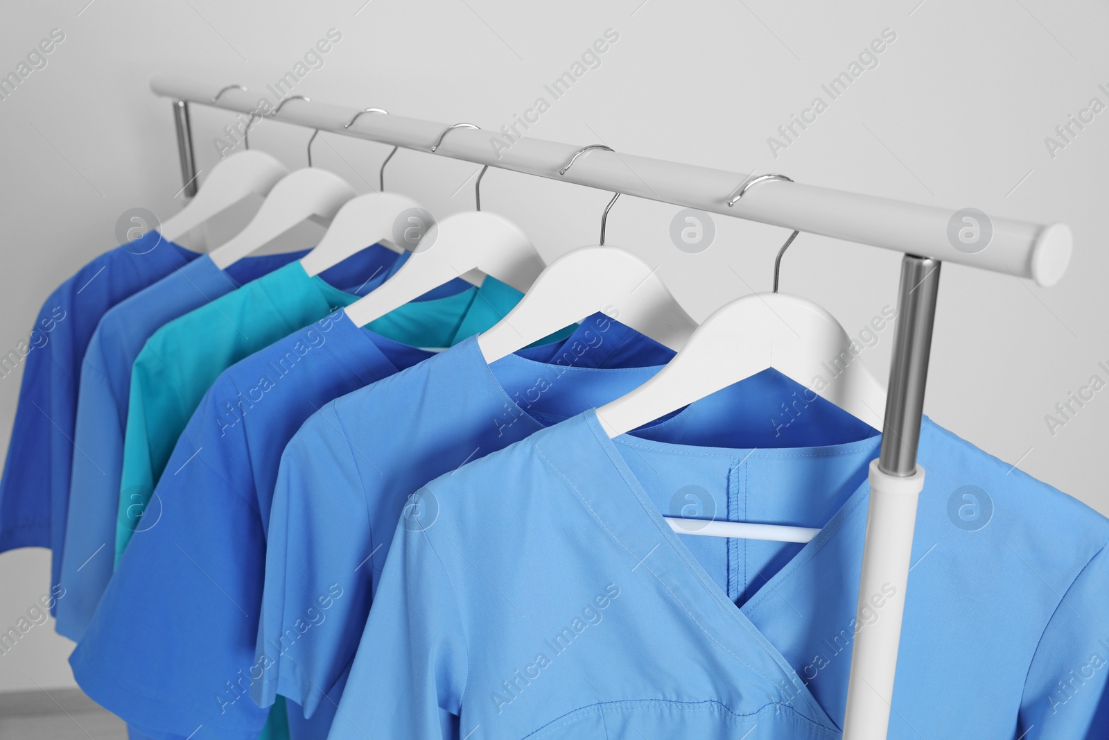 Photo of Different medical uniforms on rack against light grey background