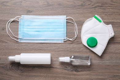 Photo of Protective masks and antiseptics on wooden background, flat lay