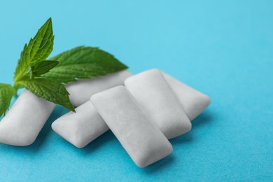 Tasty white chewing gums and mint leaves on light blue background, closeup