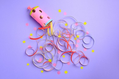 Photo of Beautiful serpentine and confetti bursting out of party popper on violet background, flat lay