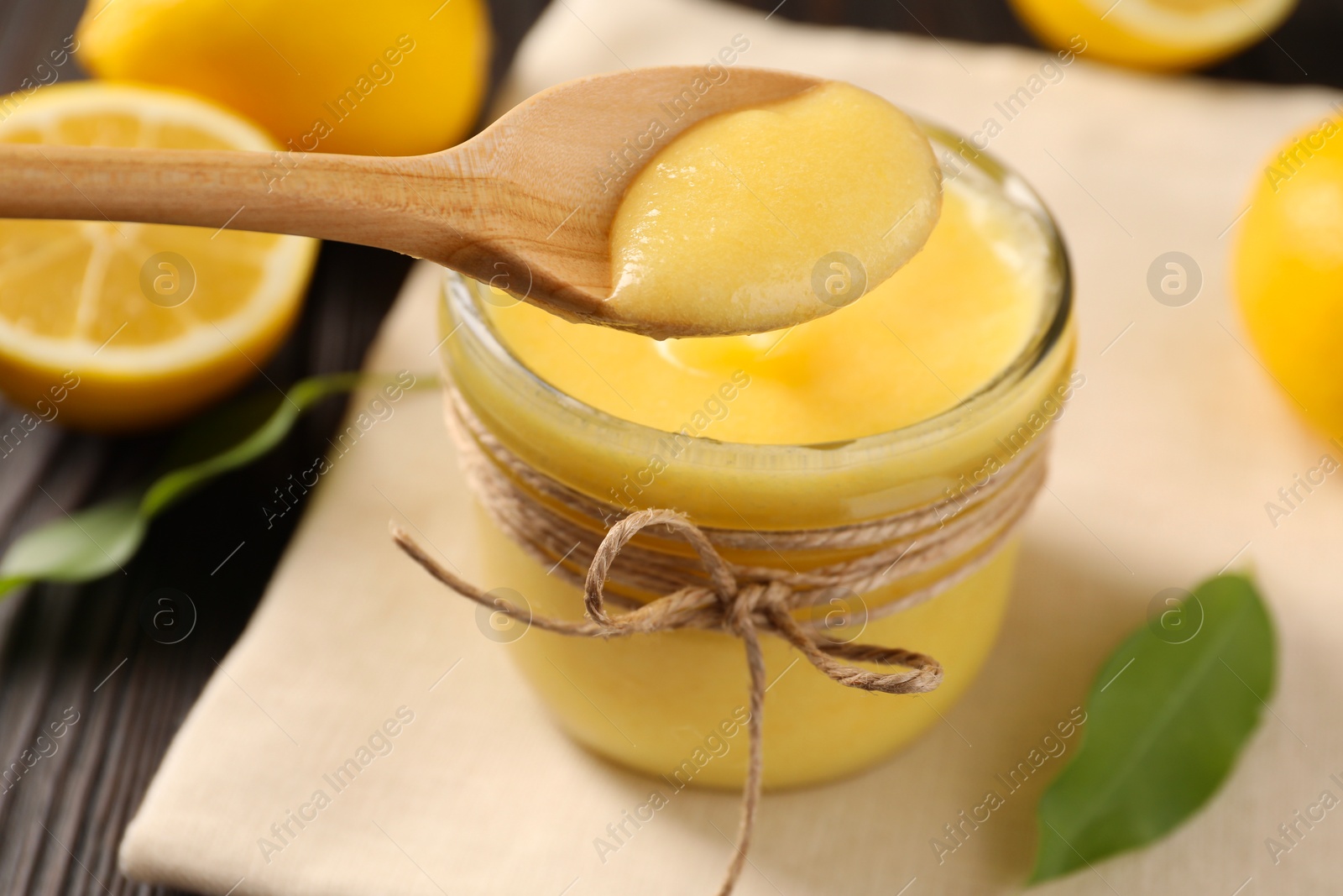 Photo of Taking delicious lemon curd from glass jar at wooden table, closeup