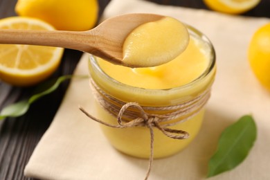 Taking delicious lemon curd from glass jar at wooden table, closeup