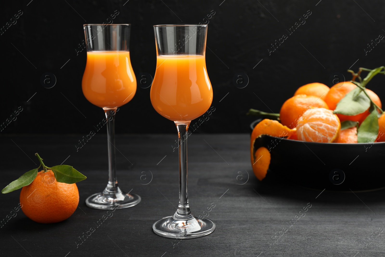 Photo of Tasty tangerine liqueur in glasses and fresh fruits on black wooden table