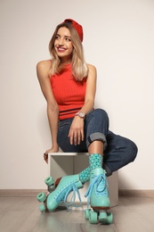 Young woman with retro roller skates against light wall