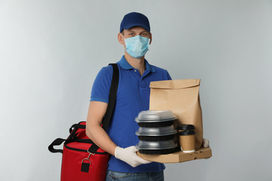 Courier in protective mask and gloves holding order on light background. Food delivery service during coronavirus quarantine