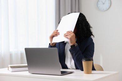 Deadline concept. Woman covering face with document in office