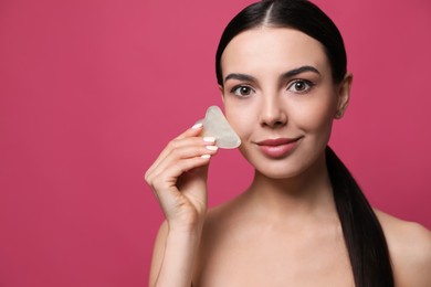 Photo of Beautiful young woman doing facial massage with gua sha tool on pink background