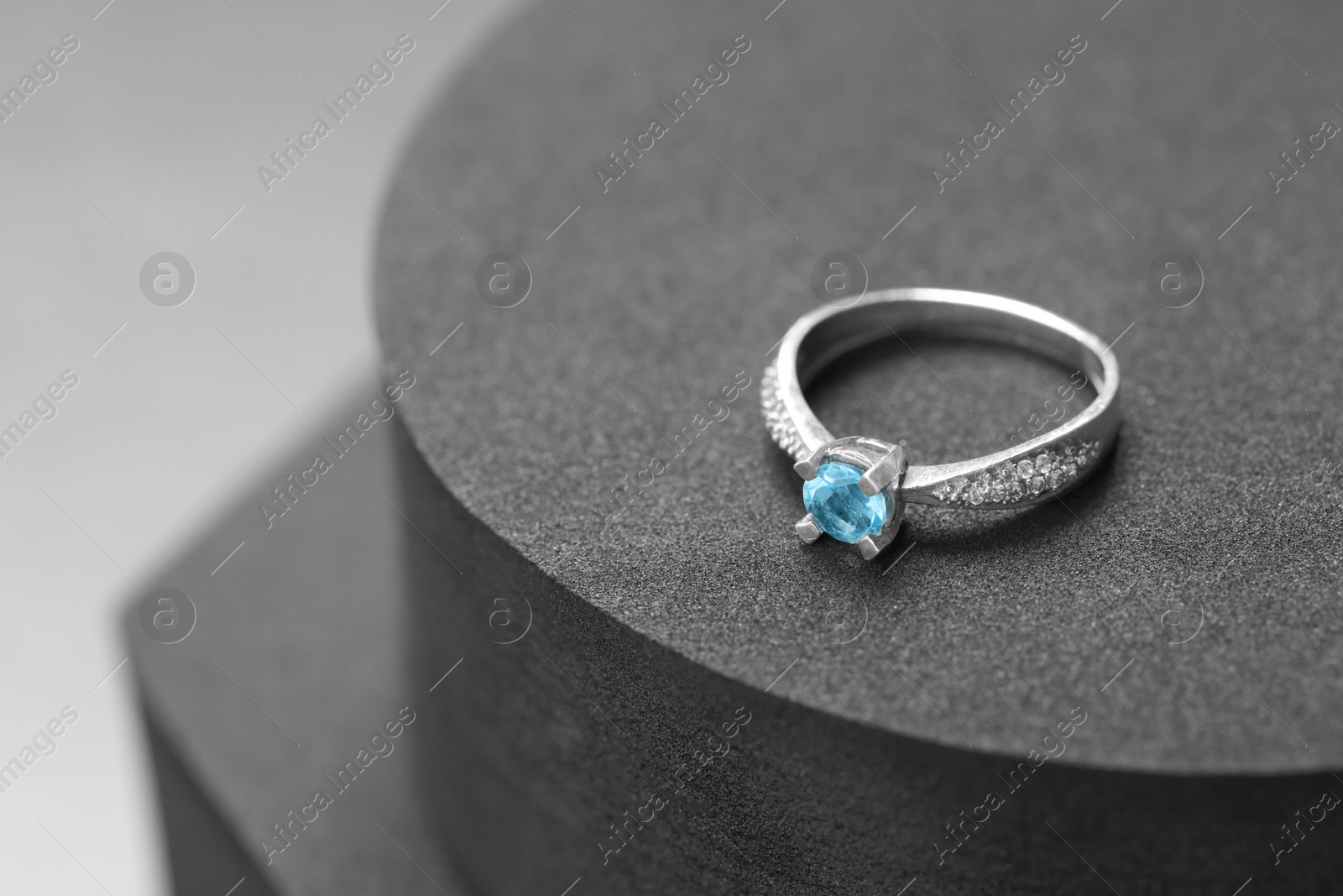 Photo of Beautiful ring with light blue gemstone on black podium, space for text. Luxury jewelry