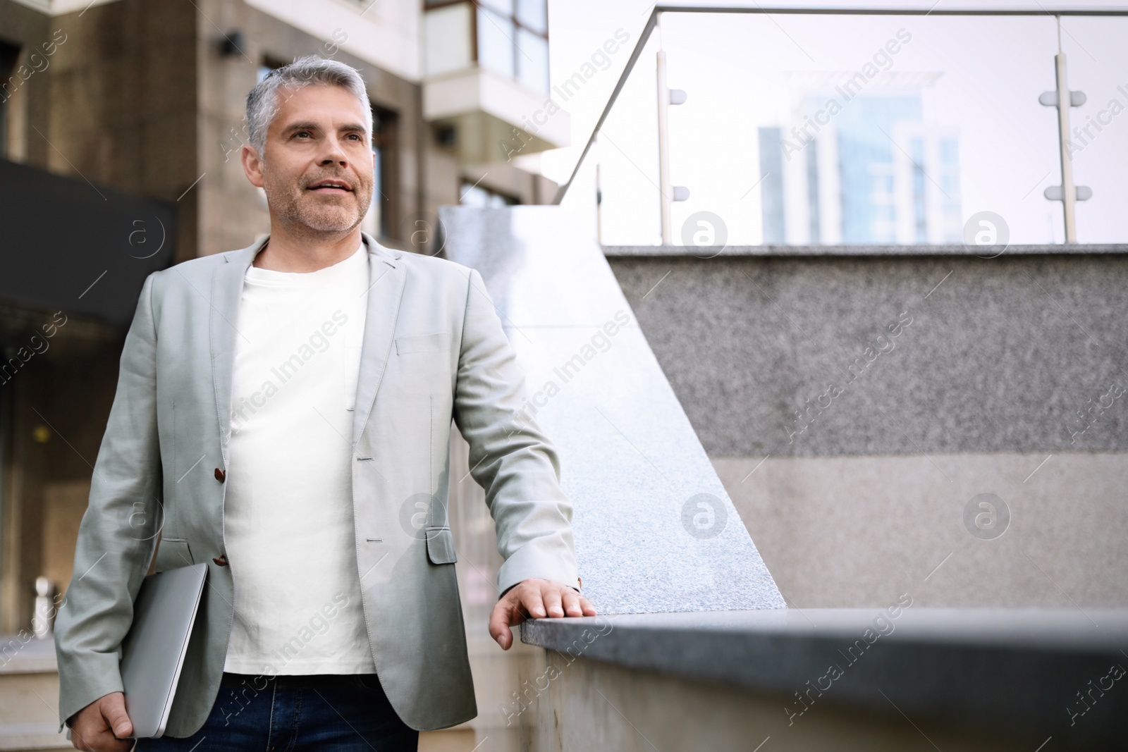 Photo of Portrait of handsome mature man with laptop in city center. Space for text