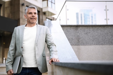 Portrait of handsome mature man with laptop in city center. Space for text