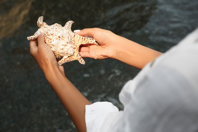 Photo of Young woman holding beautiful big seashell outdoors, closeup