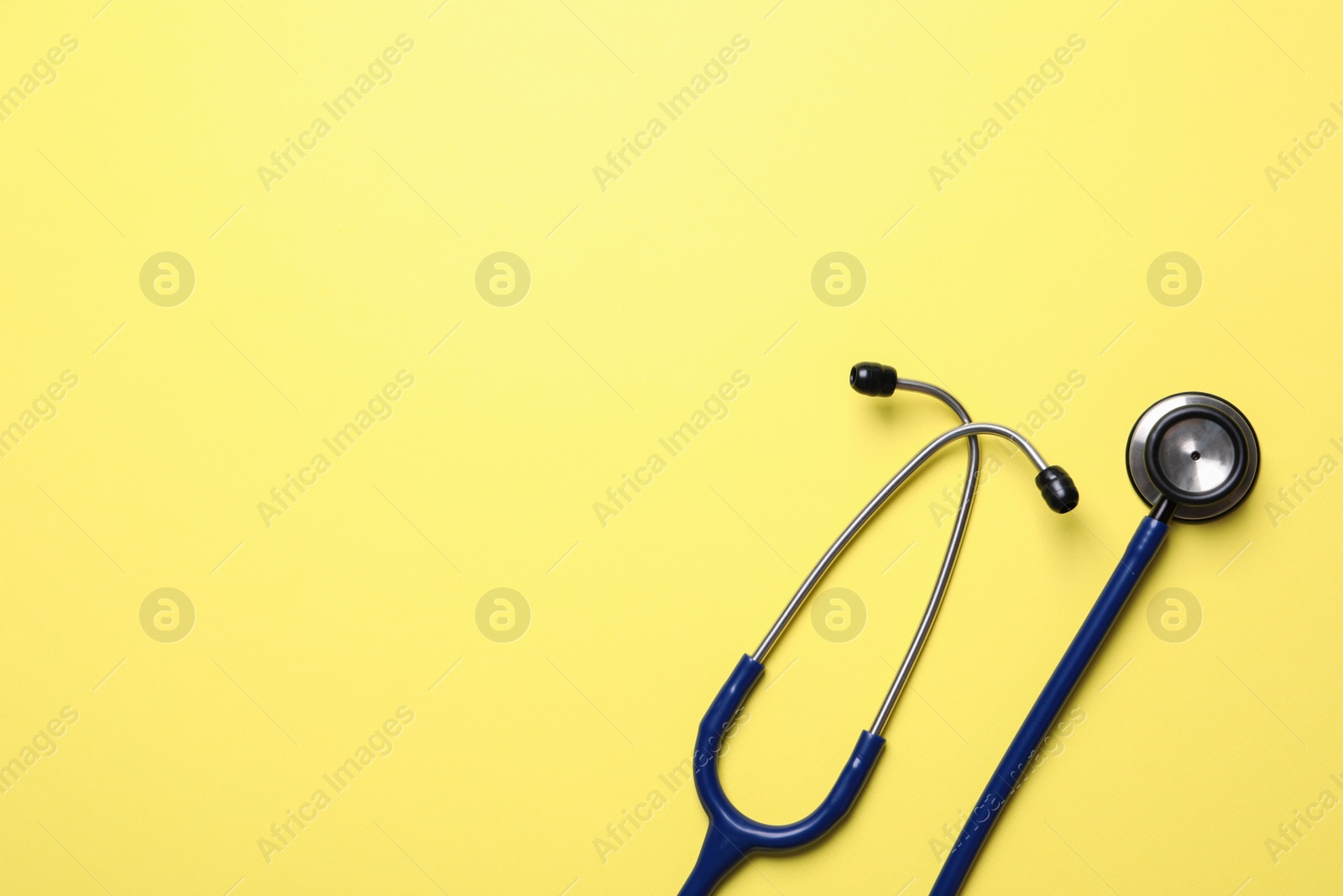 Photo of Stethoscope on yellow background, top view. Space for text