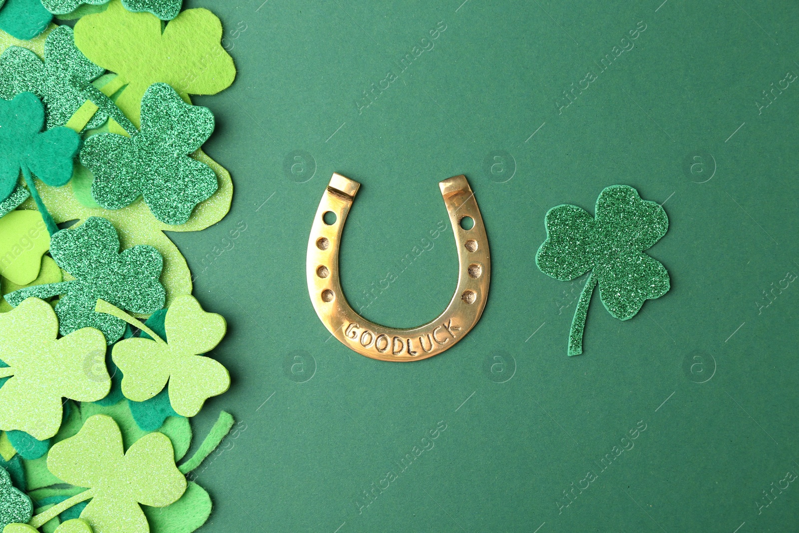 Photo of St. Patrick's day. Golden horseshoe and decorative clover leaves on green background, flat lay