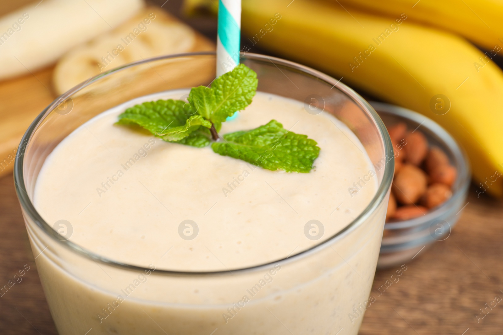 Photo of Glass with banana smoothie and mint on wooden table, closeup