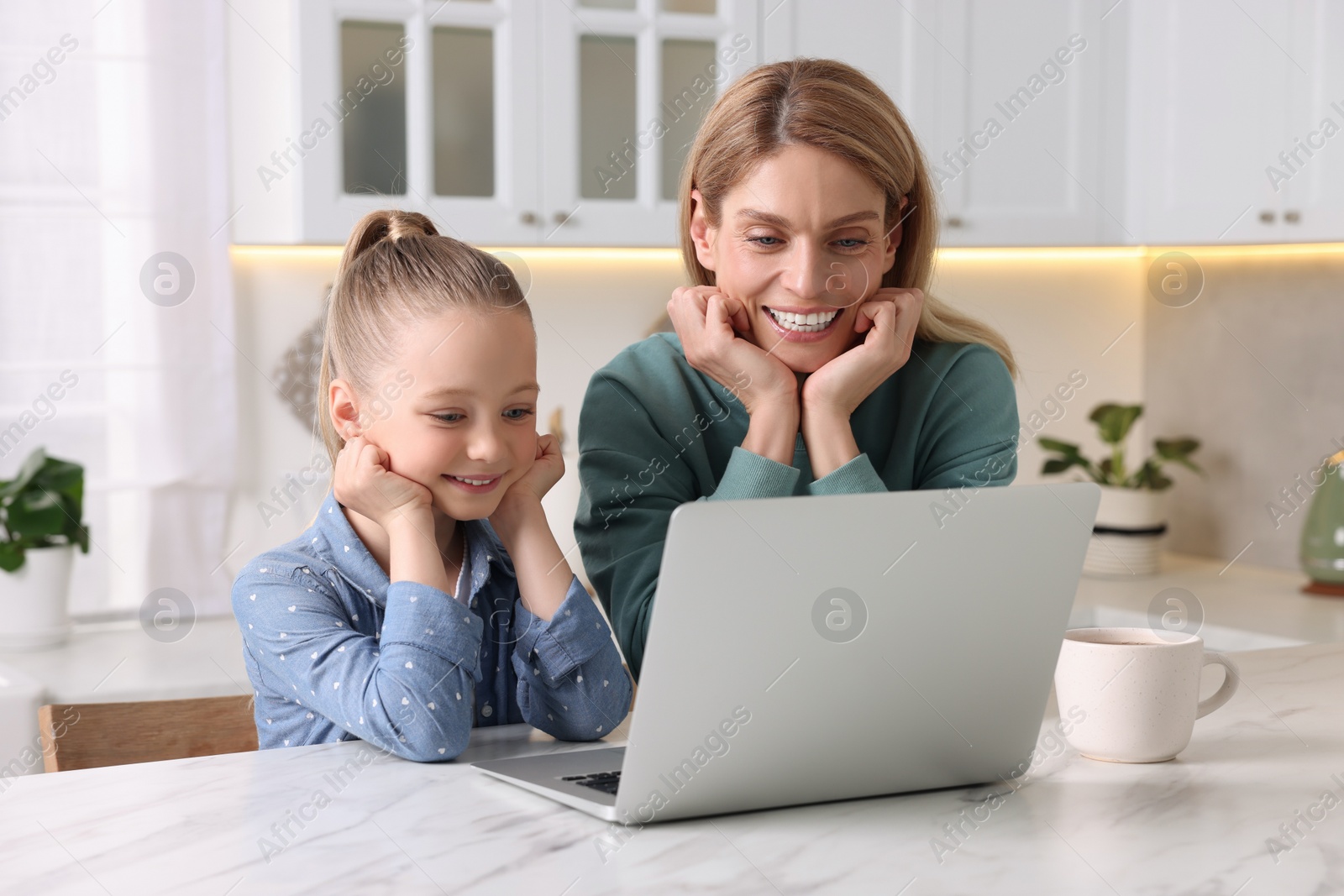 Photo of Happy woman and her daughter with laptop at white table indoors