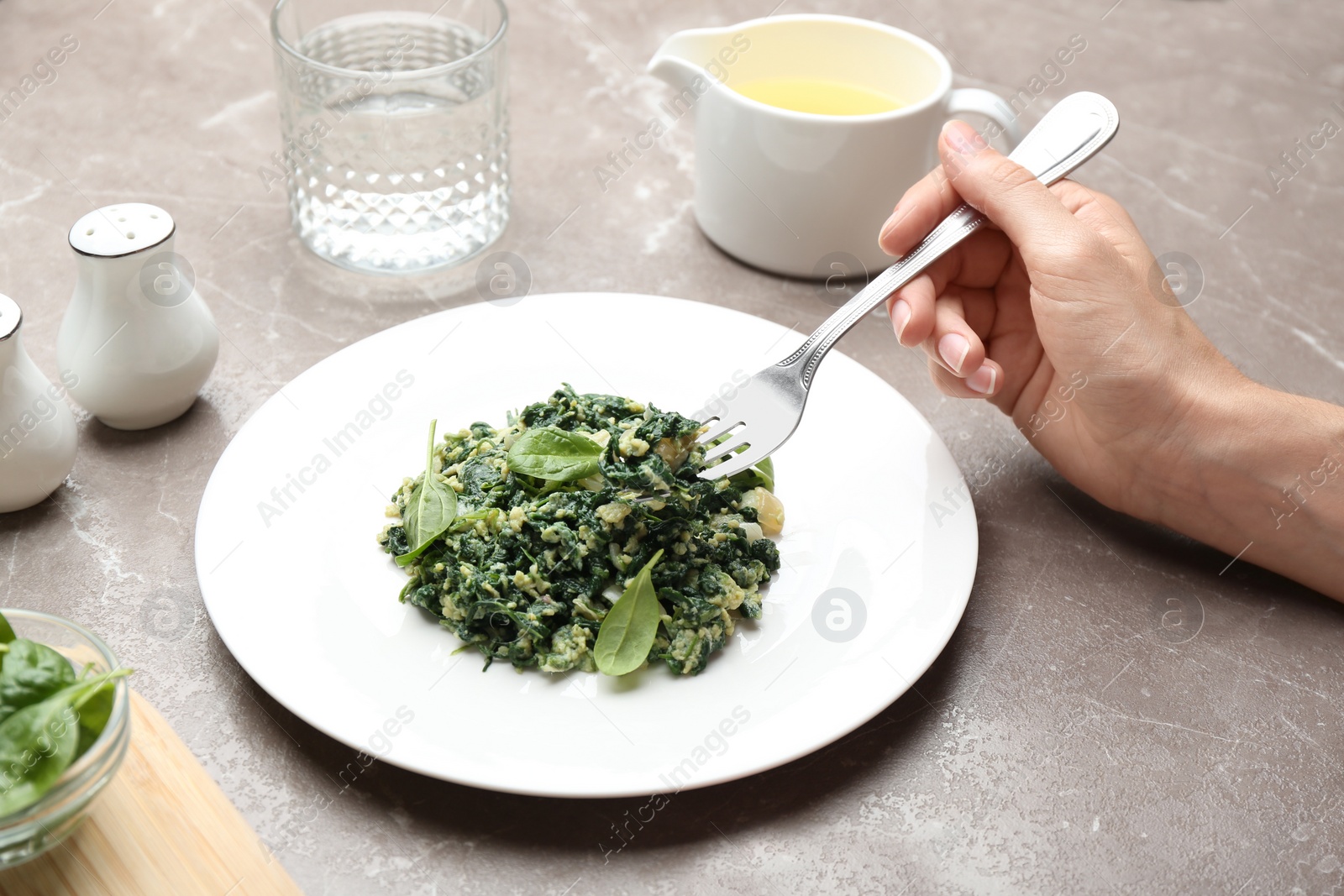 Photo of Young woman eating tasty spinach at grey marble table, closeup. Healthy food