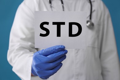 Photo of Doctor holding sheet of paper with abbreviation STD on light blue background, closeup