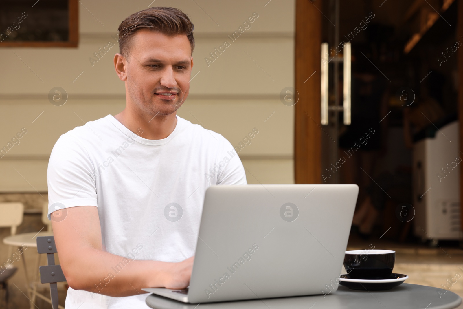 Photo of Handsome man working on laptop at table in outdoor cafe