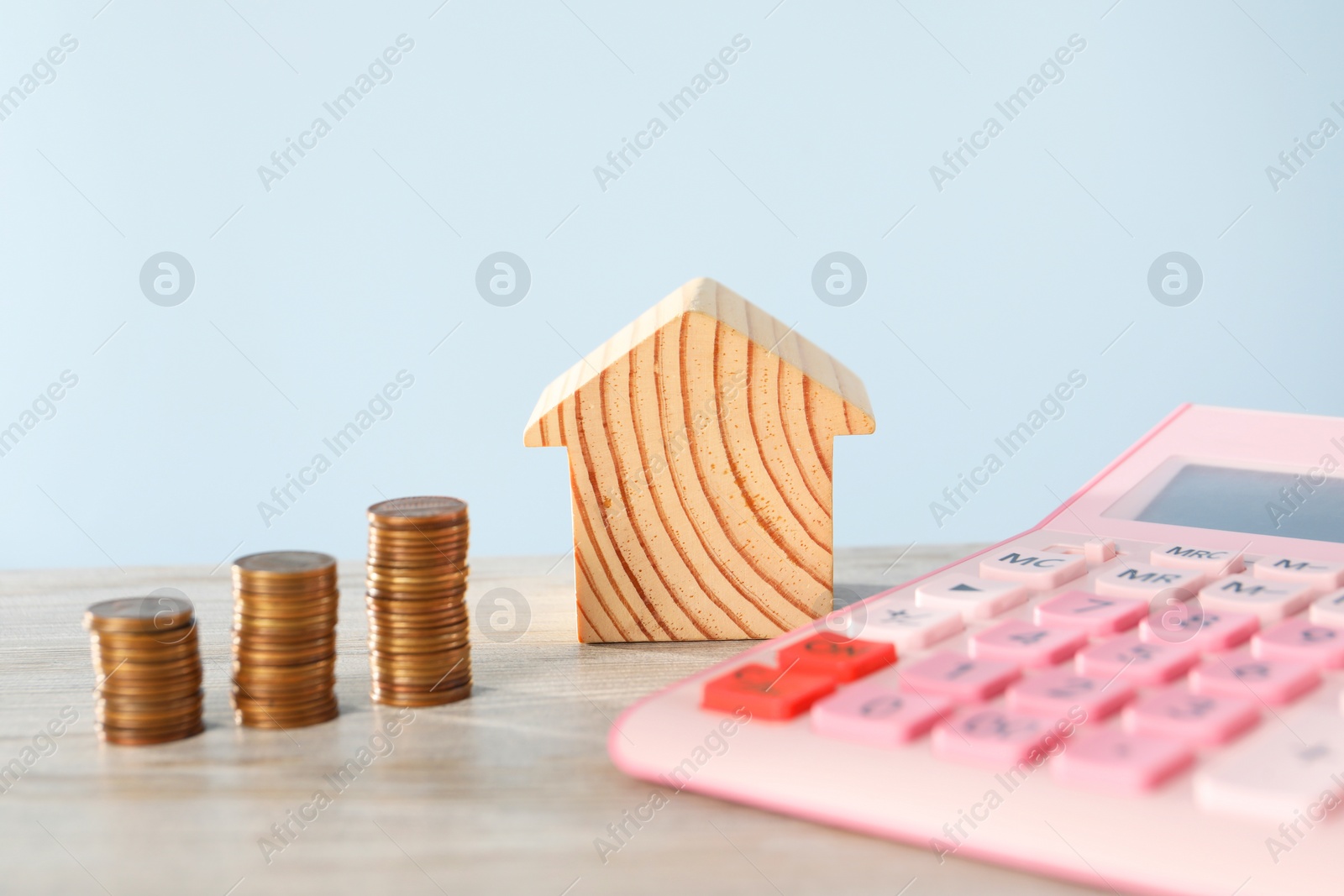 Photo of House model, calculator and coins on wooden table against light blue background