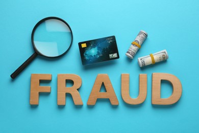 Photo of Word Fraud made of wooden letters near money, credit card and magnifying glass on light blue background, flat lay