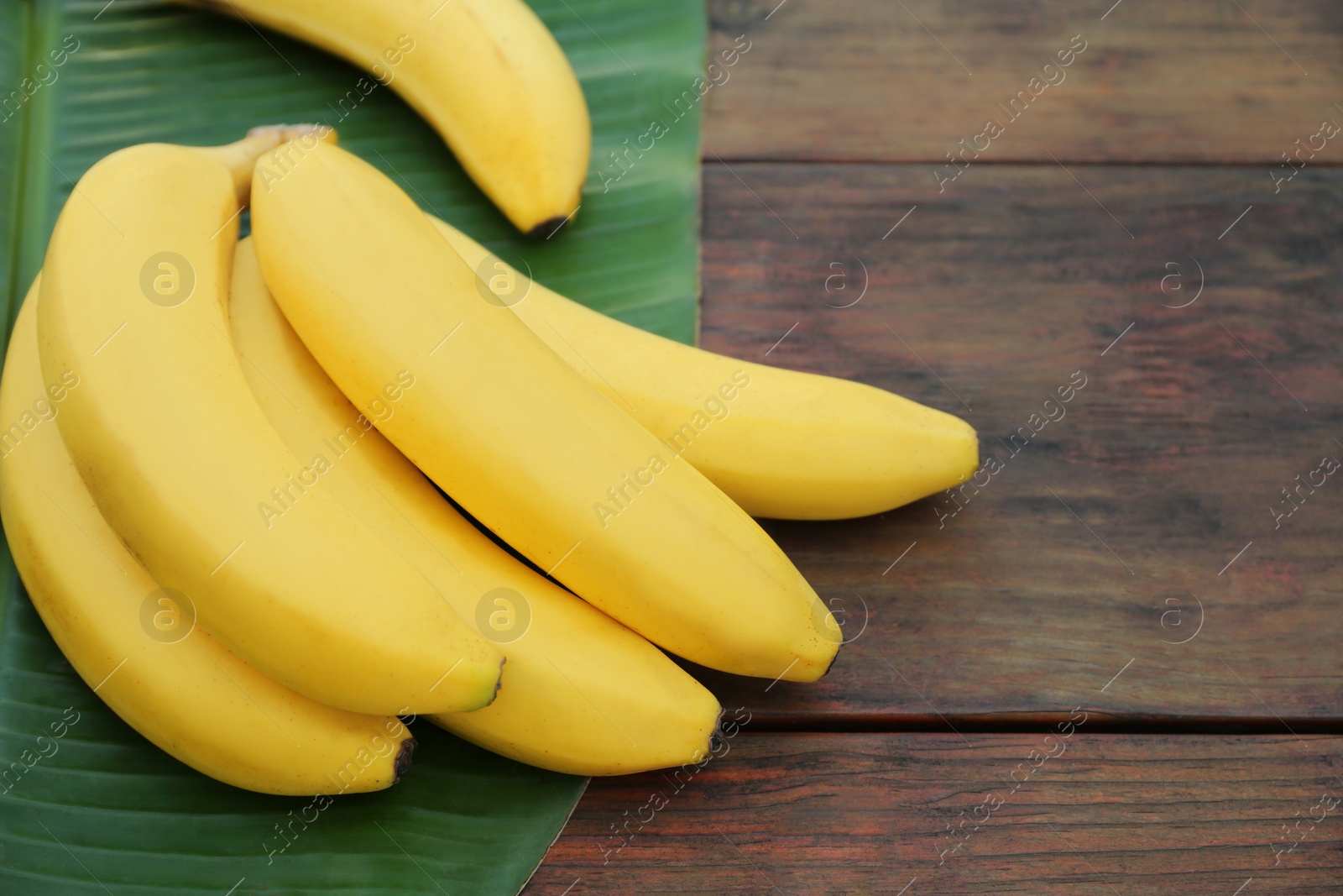 Photo of Delicious bananas and green leaf on wooden table. Space for text