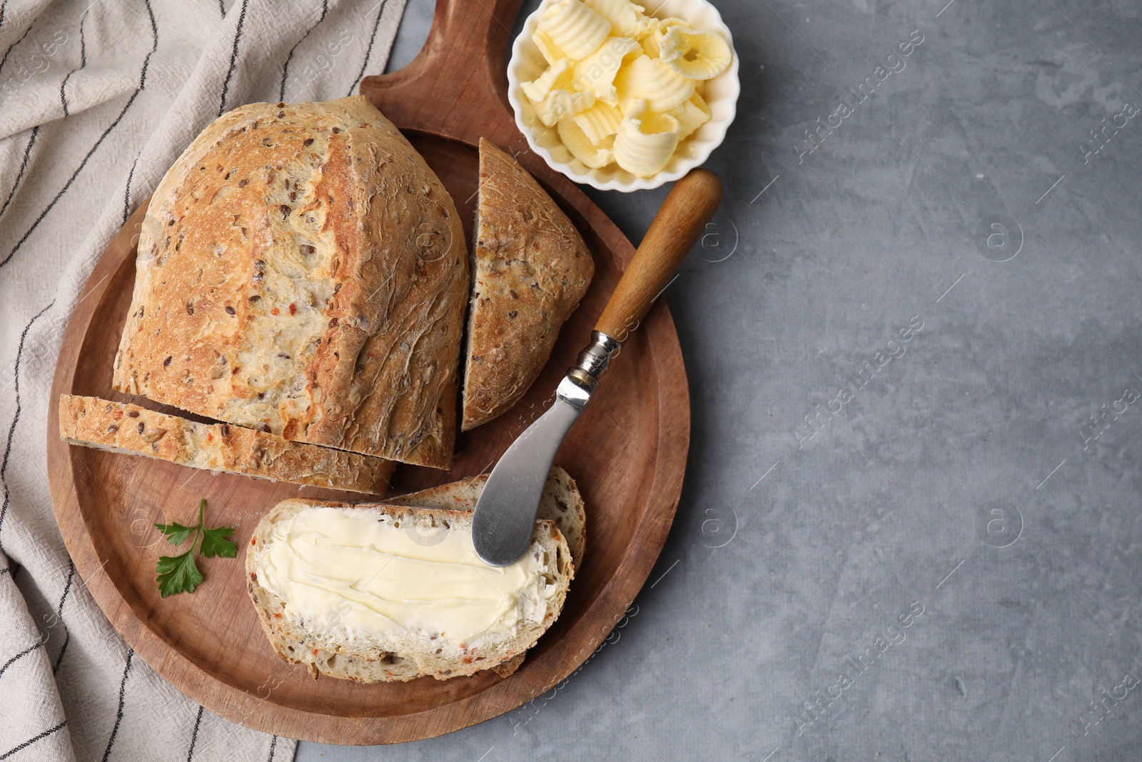Photo of Tasty bread with butter and knife on grey textured table, flat lay. Space for text
